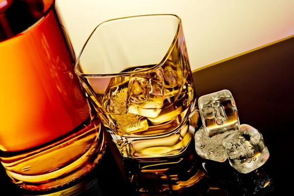 Toppen av beskåda av glas whiskey nära flaskan och isbitar på bord med eftertanke — Stockfoto