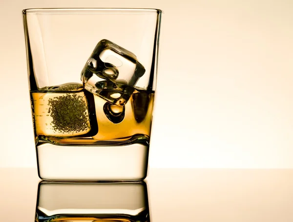 Un vaso de whisky con cubitos de hielo en la mesa con reflexión, atmósfera marrón claro — Foto de Stock