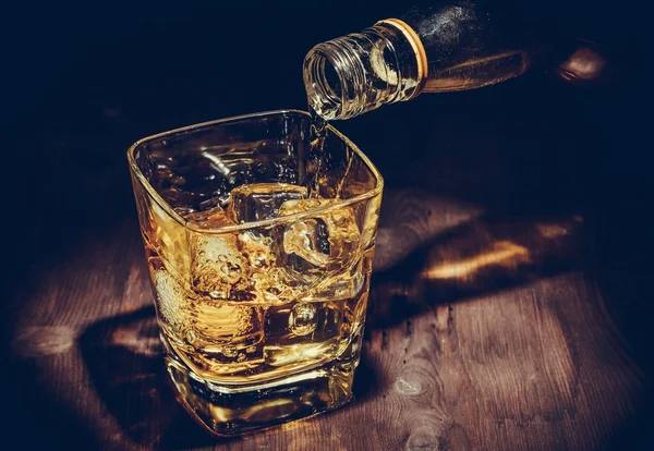Barman, nalil whisky sklenice na dřevěný stůl, vřelou atmosféru, starý styl — Stock fotografie