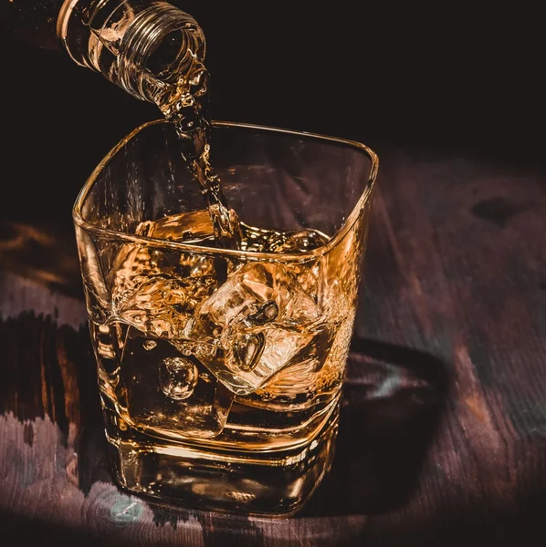 Barman verter whisky en el vaso en la mesa de madera, ambiente cálido, estilo antiguo, tiempo de relax con whisky — Foto de Stock