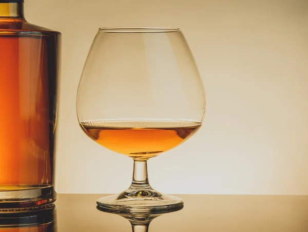 Snifter brandy w eleganckim typowym koniak szkło w pobliżu butelki na stole, ciepłym stylu — Zdjęcie stockowe