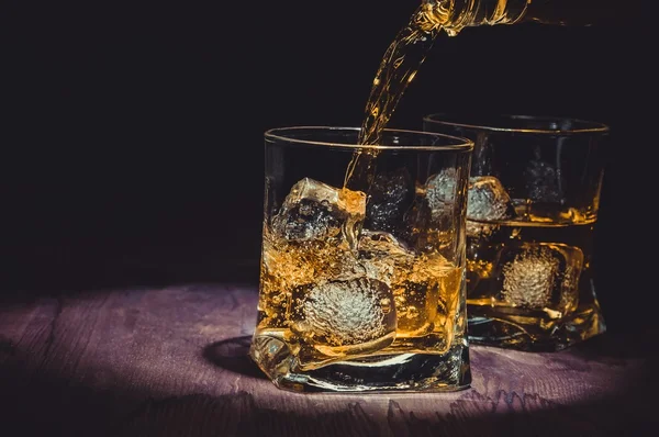 Barman verter whisky en dos vasos en la mesa de madera, ambiente cálido, estilo antiguo, tiempo de relax con whisky — Foto de Stock