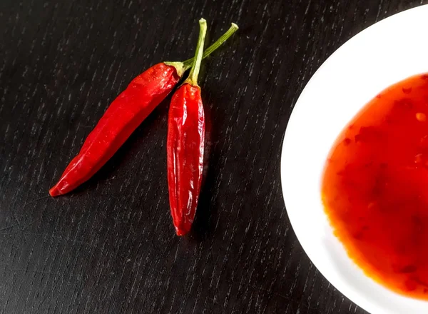 Spicy hot tomato sauce as a snack or appetizer in a white disc near spicy peppers — Stock Photo, Image