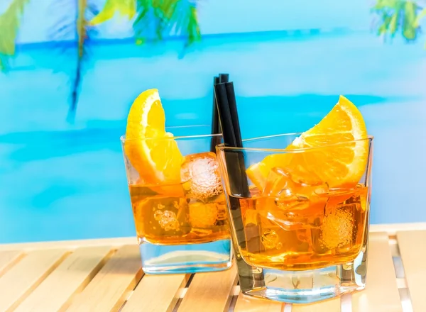 Dwie szklanki aperol aperitifem spritz koktajl z plastrami pomarańczy i kostki lodu na rozmycie tła plaża i palmy — Zdjęcie stockowe