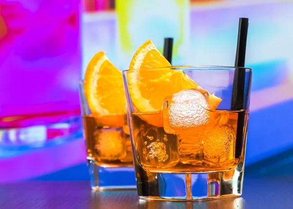 Dwie szklanki aperol aperitifem spritz koktajl z plastrami pomarańczy i kostki lodu na pasku tabela, dyskoteka atmosfery tło — Zdjęcie stockowe
