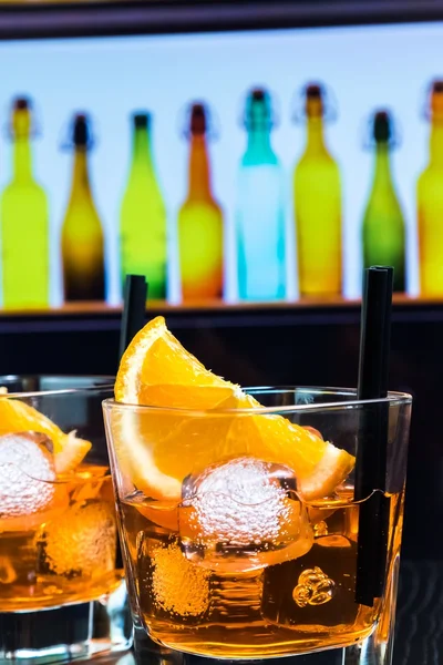 Detail ze dvou sklenic spritz aperol aperitiv koktejl s FILÁTKY a kostky ledu na panel tabulka, disco atmosférou pozadí — Stock fotografie