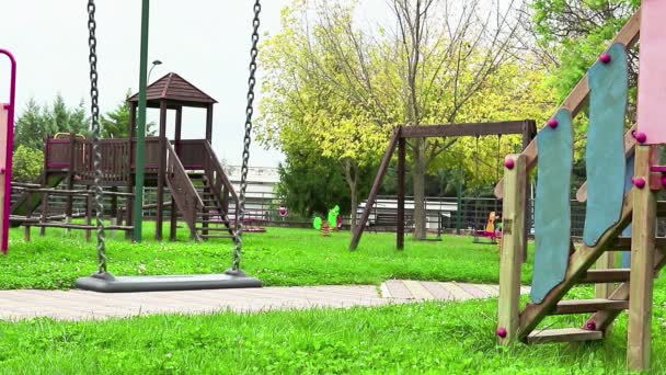 Порожні гойдалки з ланцюгами, що ширяють на дитячому майданчику, переміщені з вітру, на зеленому фоні лугу в повільному циклі руху — стокове відео