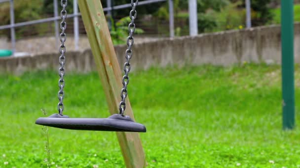 Columpio vacío con cadenas balanceándose en el patio de recreo para el niño, movido del viento, sobre fondo verde del prado — Vídeos de Stock