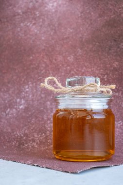 glass jar with honey on a Burgundy background. Glass jar with sweet honey