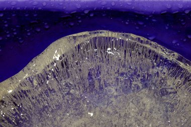 Pure transparent rectangular ice block with air bubbles on purpure background.