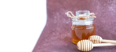 banner glass can full of honey and wooden stick on it on a burgundy background with space for your text