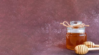 banner glass can full of honey and wooden stick on it on a burgundy background with space for your text