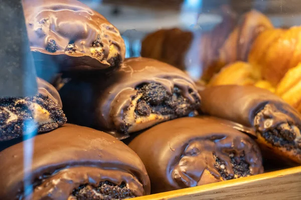 buns with poppy seeds and chocolate on sale in the window. Poppy seed roll covered with chocolate glaze close up on a marble background, horizontal orientation