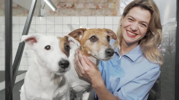 Веселая женщина-ветеринар улыбается в камеру, гладя милых собак — стоковое видео