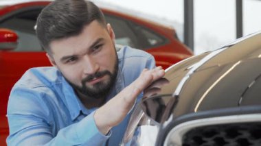 Galeride yeni bir arabayı incelerken kameraya gülümseyen yakışıklı adam.