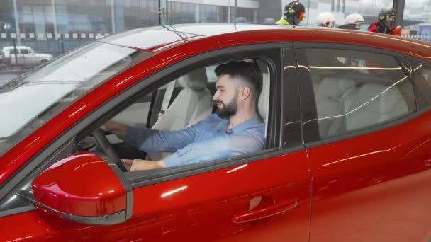 Attraktiver junger Mann lächelt in die Kamera, als er im Autohaus in einem Neuwagen sitzt — Stockvideo