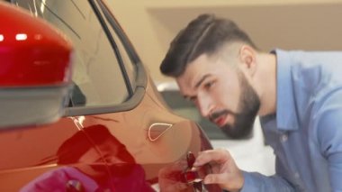 Kırmızı otomobili inceleyen yakışıklı sakallı adam.