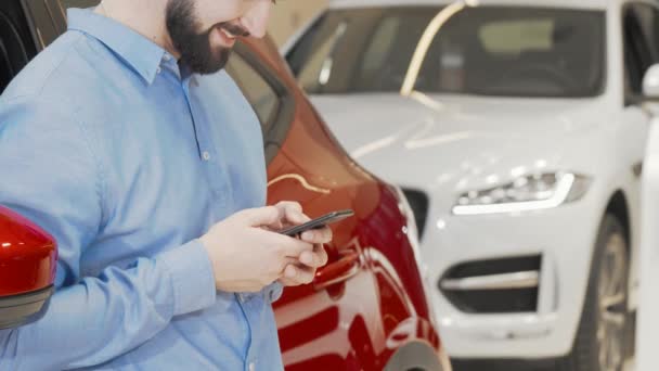 Tiro cortado de um homem feliz usando telefone inteligente na concessionária de carros — Vídeo de Stock