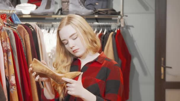 Νεαρή γυναίκα εξετάζει ψηλοτάκουνα παπούτσια στο κατάστημα μόδας — Αρχείο Βίντεο