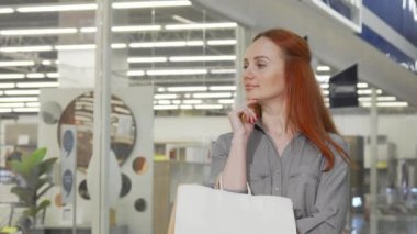 Alışveriş merkezinde alışveriş yaparken kameraya gülümseyen neşeli kadın.