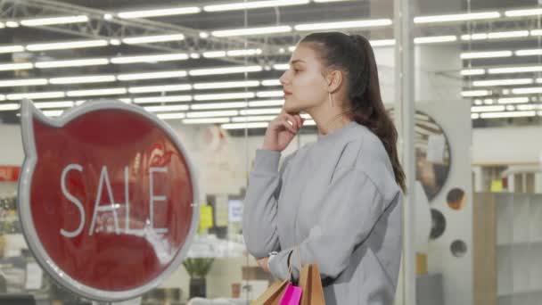 Jovem mulher olhando para a exibição de uma loja no shopping — Vídeo de Stock