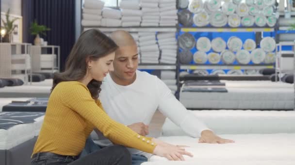 Szczęśliwa para badająca materac ortopedyczny na sprzedaż w sklepie z meblami — Wideo stockowe