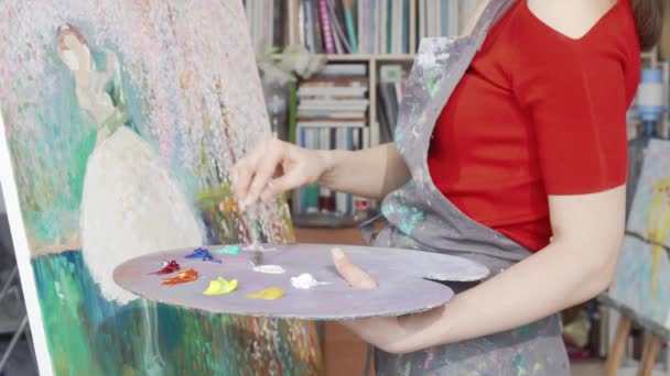 Gehakte foto van een vrouwelijke kunstenaar mengen verf op haar palet tijdens het tekenen — Stockvideo