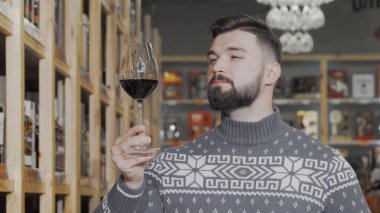 Yakışıklı adam şarap süpermarketinde kırmızı şarap tadıyor.