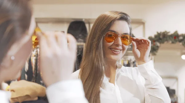 Υπέροχη νεαρή γυναίκα δοκιμάζει νέα γυαλιά ηλίου στο κατάστημα μόδας Φωτογραφία Αρχείου