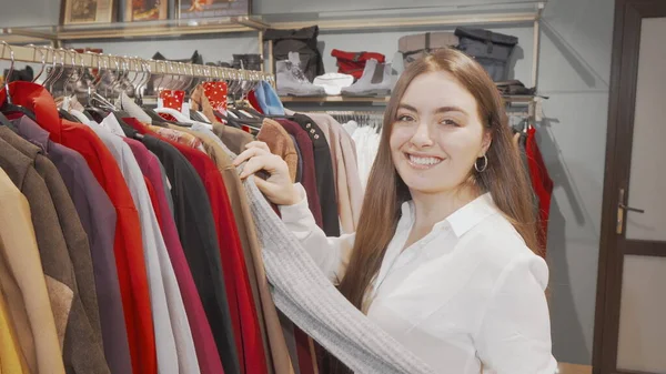 Χαρούμενη γυναίκα που εξετάζει ρούχα προς πώληση στο κατάστημα μόδας Εικόνα Αρχείου