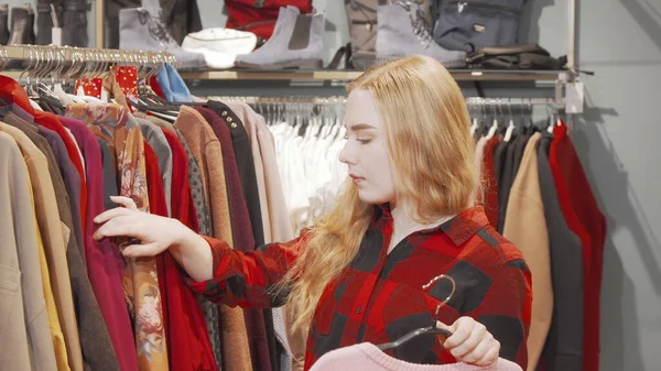 Молодая женщина выбирает одежду, чтобы попробовать в магазине моды Лицензионные Стоковые Фото