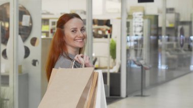 Alışveriş merkezinde alışveriş yaparken kameraya gülümseyen mutlu kadın.