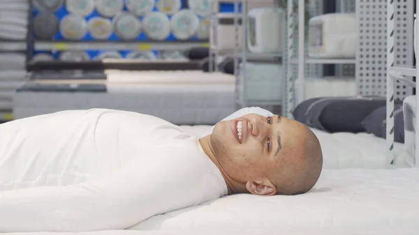 Mutlu Afrikalı adam mobilya mağazasında ortopedik yatakta yatıyor. Stok Fotoğraf