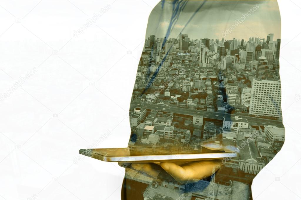 Double exposure of a businessman and a city using a tablet over 
