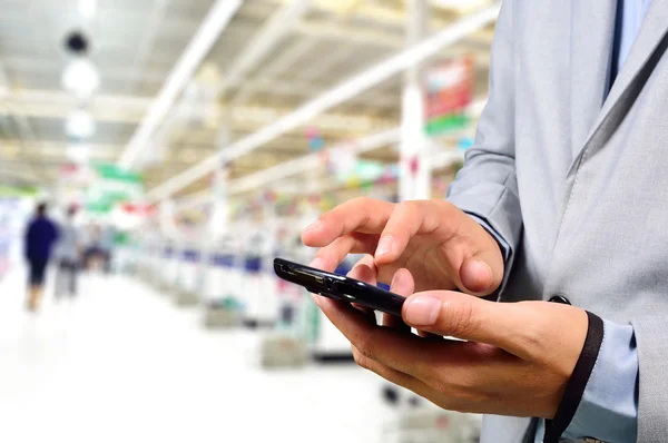 Hombre de negocios usando el teléfono móvil mientras hace compras en el supermercado . —  Fotos de Stock