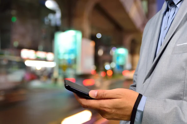 Geceleri şehirde akıllı telefon kullanan yakışıklı bir adam.