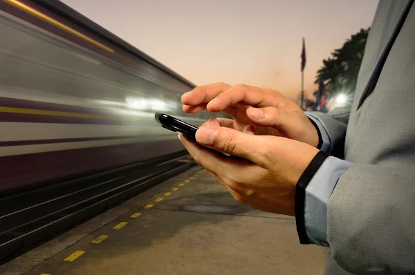 Obchodní muž použít mobilní telefon v železniční stanici za svítání — Stock fotografie