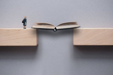 Kadın minyatür figürün geçebilmesi için tahta bloklar arasındaki boşluğu kapatan açık bir kitap. 