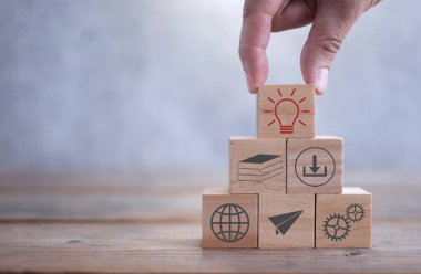 Ampul sembolü, çeşitli eğitim ve e-öğrenim simgelerine sahip ahşap yapı taşlarından bir kuleye yerleştiriliyor.