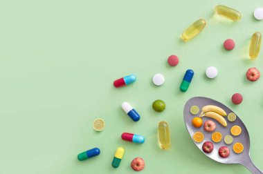 Elma, muz, kireç ve portakalların yanı sıra vitamin hapları ve kapsüller içeren kaşık.