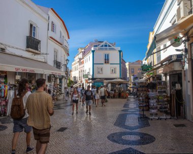 Lagos, Portekiz - 21 Eylül 2025: Portekiz 'in eski Lagos kentindeki Rua 25 de Abril' in güzel bir manzarası. Cadde restoranlar, butikler ve hediyelik eşya dükkanlarıyla dolu..