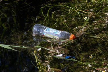 Kirlenmiş bir nehirde, bir su şişesine yakın çekim.