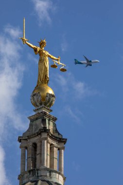 Londra, İngiltere - 20 Ağustos 2024: Londra 'daki Old Bailey' nin tepesindeki Adalet Heykeli. Arka planda bir Aer Lingus uçağı uçuyor..