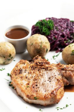 Alman usulü ızgara domuz pirzolası, ekmek köftesi ve beyaz arka planda geleneksel kırmızı lahana yemeği.