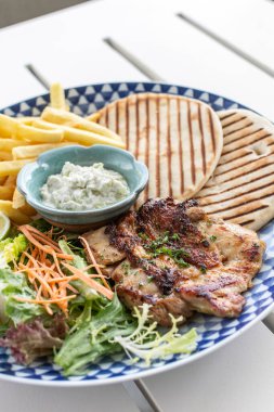 Yunan usulü ızgara tavuk göğsü. Patates kızartması ve salata. Açık havada, Yunan restoranının beyaz masasında.