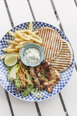 Yunan usulü ızgara tavuk göğsü. Patates kızartması ve salata. Açık havada, Yunan restoranının beyaz masasında.