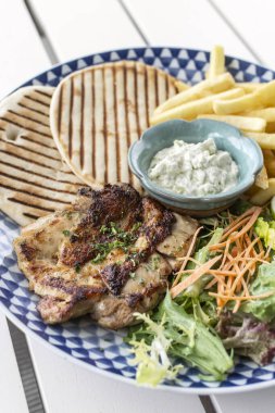 Yunan usulü ızgara tavuk göğsü. Patates kızartması ve salata. Açık havada, Yunan restoranının beyaz masasında.