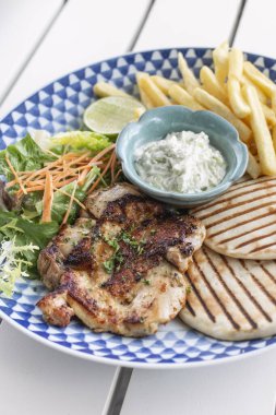 Yunan usulü ızgara tavuk göğsü. Patates kızartması ve salata. Açık havada, Yunan restoranının beyaz masasında.