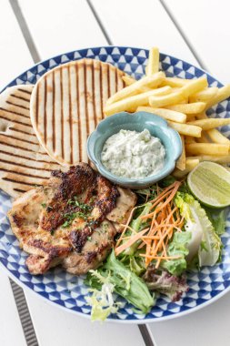 Yunan usulü ızgara tavuk göğsü. Patates kızartması ve salata. Açık havada, Yunan restoranının beyaz masasında.