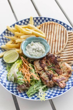 Yunan usulü ızgara tavuk göğsü. Patates kızartması ve salata. Açık havada, Yunan restoranının beyaz masasında.